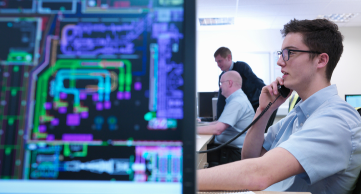 Close up of computer screen with a man working at a desk in the background