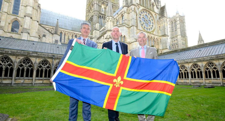 Three leaders at Lincoln Cathedral holding a Lincolnshire flag